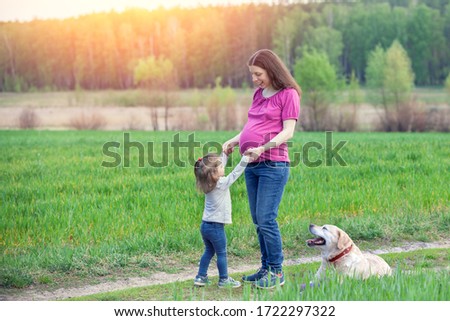 Young happy pregnant woman with little daughter outdoors in summer.  A dog lying nearby. Mother's Day concept