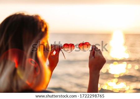 young woman looking through sunglasses in the shape of a heart on the sea. concept of love to sea