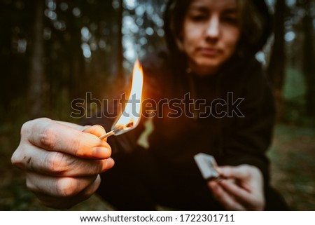 Teenage bully in hood holds burning match in his hand. Forest arsonist. Fire danger. Concept of arson and flame in night Royalty-Free Stock Photo #1722301711