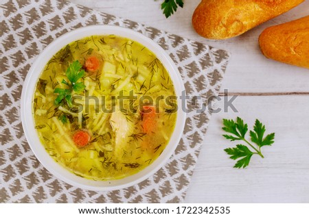 Bowl of chicken noodle soup with bread on white table.