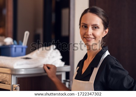 A portrait of a smiling hotel maid with a cleaning cart and clea Royalty-Free Stock Photo #1722347302