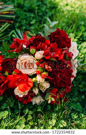 Beautiful red wedding bouquet of the bride lies on the green grass. Outdoor wedding ceremony. Wedding day. Closeup details of a wedding decor