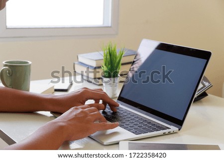 A man uses a laptop at home while sitting at a wooden table. Man hands typing on a notebook keyboard. The concept of young people working at mobile devices.