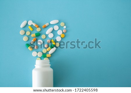 colorful pills and capsules in the shape of a heart from a jar on a blue-green background, located on the left side of the image, with a free area for text, love