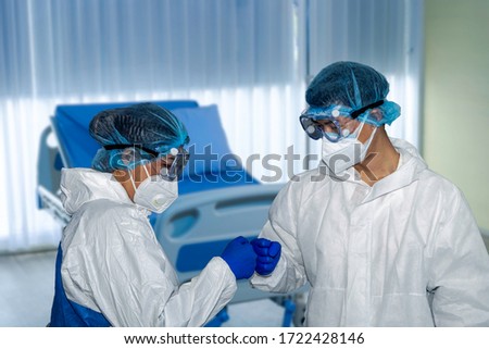 Two medical staff in blue gloves and white hygiene covers are celebrating by fist bump to each other in a hospital after a successful case of recovery from sickness. Good team spirit and friendship