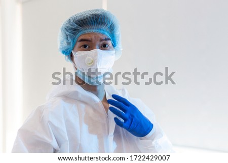 Asian male medical doctor in personal protective equipment suit is taking rest after long hours operation helping patients to get better. Man in disposable protective cover, hygiene gloves and mask