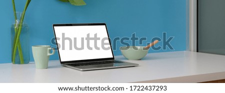 Cropped shot of creative workspace with blank screen laptop, breakfast meal and copy space on white table with light blue wall