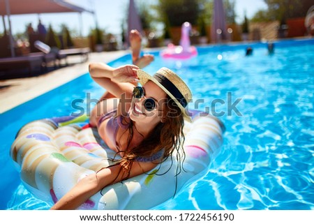 Young smiling fitted girl in bikini, straw hat relax on inflatable swan in swimming pool. Attractive woman in swimwear lies in the sun on tropical vacation. Pretty female sunbathing at luxury resort. Royalty-Free Stock Photo #1722456190