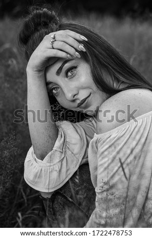 An attractive young woman frames her face with her lower arm and hand during an outdoor summer portrait near Liverpool.