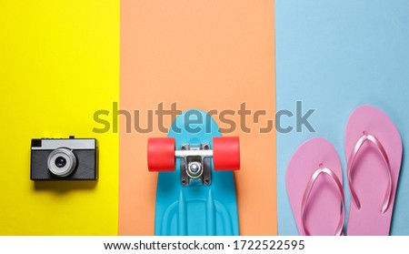Hipster outfit. Skateboard with retro camera, flip flop on colored background. Creative fashion minimalism. Trendy old fashionable style. Minimal summer fun. Music concept. Top view