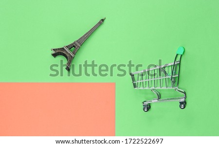 Shopping in Paris minimalistic concept. Shopping trolley, eiffel tower figurine on pastel colored background. Top view