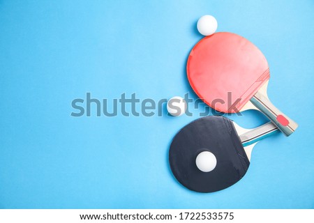 Table tennis rackets and a white plastic balls on a blue background.