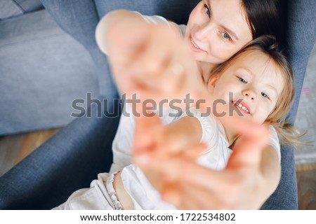 a young mother with her daughter sit on a chair and show their hands out the window