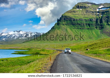 White cars running on a curved road The background is a great mountain with green grass all over the area. During the summer in Iceland, Road trip concepts and driving in traveling.