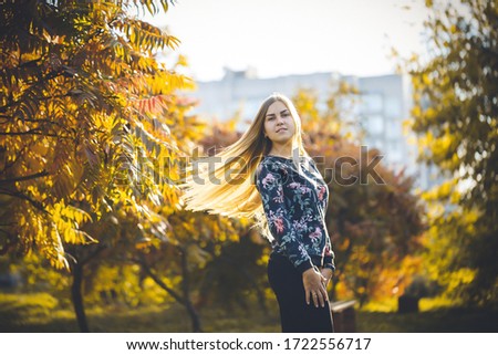 Woman girl long-haired blonde in an alley with trees with red leaves. She is happy confident in a photo shoot. Autumn park sunny warm day.