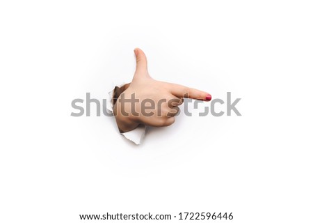 The thumb and forefinger points to the right side. White background and place for advertising with copy space. The child's hand came out into the torn paper hole.