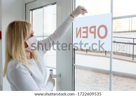 Business office or store shop is open business of novel Coronavirus COVID-19 pandemic. Unidentified person wearing mask hanging open sign in background on front door.