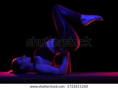 Young fit woman practicing yoga. Neon light. Modern sci fi representation of yoga.
