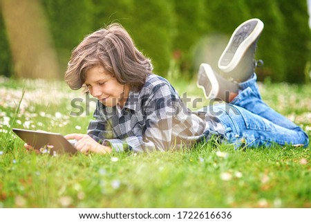 Leisure time, child boy using digital tablet while lying in green spring garden