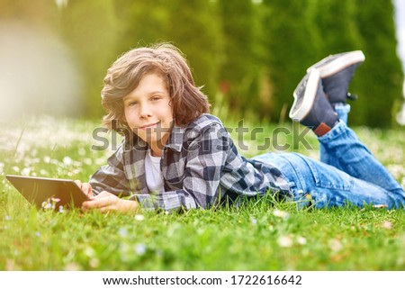 Leisure time, child boy using digital tablet while lying in green spring garden