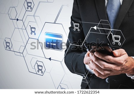 Unrecognizable businessman holding smartphone over blurry gray background with double exposure of futuristic online shopping and banking interface. Toned image