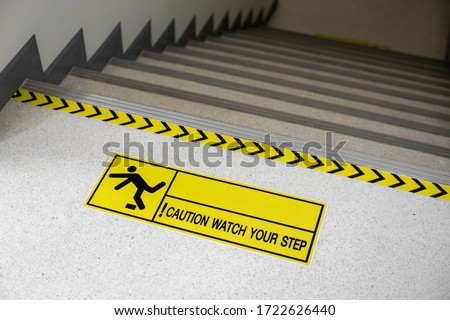 Yellow and black warning sign on stairs stating "Watch your Step" signifying a potential trip hazard, steep stairs and care to be taken when going up or down stairs