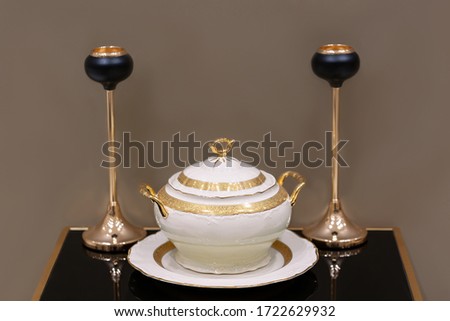 selective focus of luxury porcelain tureen with gilding from exclusive dinner set, two candle holders on a black glass table. Royalty-Free Stock Photo #1722629932