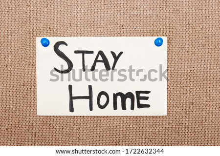 Adhesive note with Stay Home text attached to the bulletin board by pushpins