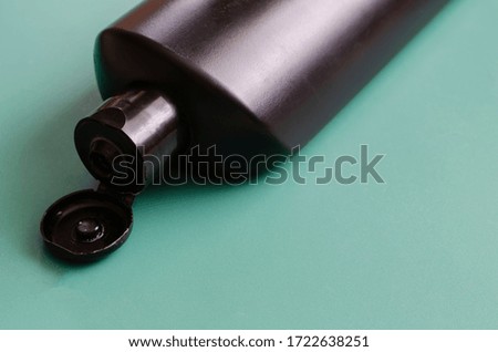 Black plastic bottle with an open cap on a turquoise background. Black bottle of shampoo or shower gel. Side view. Close-up. Selective focus. Free space for designer text.