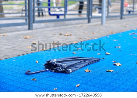Autumn in city, closeup of an umbrella and fallen first yellow leaves, blue surface of the playground background