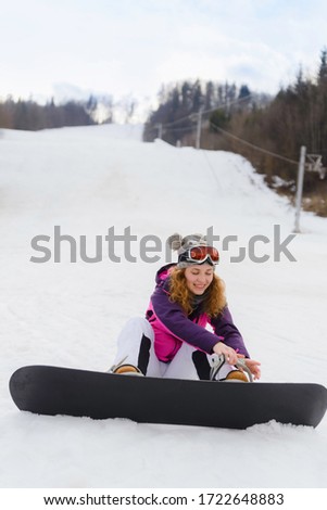 Young woman strapping on her snowboard at ski slope