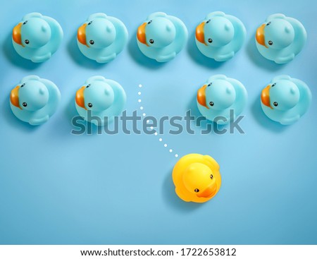 Group of blue toy ducks floating in one direction and one yellow toy duck floating in different way on blue background. Business innovative concept.