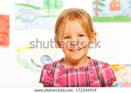 Happy smiling close portrait of cute blond little girl in the class in kindergarten with images on background