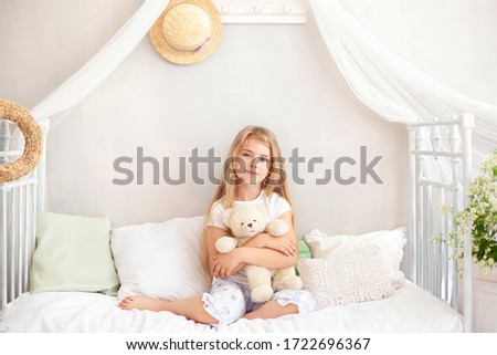 Cute blonde little girl hugs teddy bear, copyspace. Childhood concept. Child play teddy bear, look at camera and smiling while sitting on bed. Little girl smiling in pajamas in bedroom. sleep time. 
