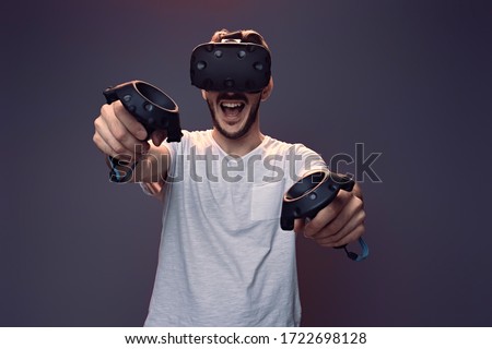 Technology, gaming, entertainment and people concept - happy young man with virtual reality headset or 3d glasses with controller gamepad playing video game in studio isolated neon purple