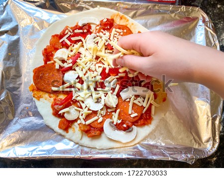 A child's hand sprinkles grated cheese on homemade pizza.