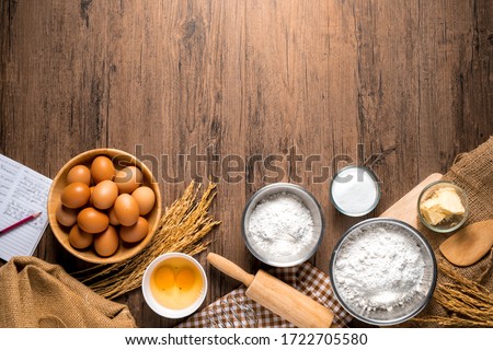 Pictures of ingredients for making cakes bakery around, such as eggs, flour, sugar, butter, recipe book and equipment for making on a wooden floor, with copy space.