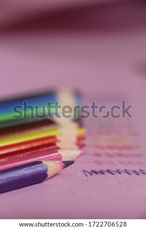 Multicolored pencils on the pink paper. Colorful zigzag lines and colored pencil. Purple, pink, red, orange, yellow, brown, green, blue and black pencils. Blurred background.