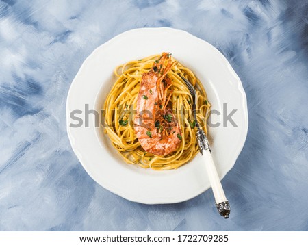 Linguine pasta with tiger prawn sauce in white dish over blue and white background. Seafood dish