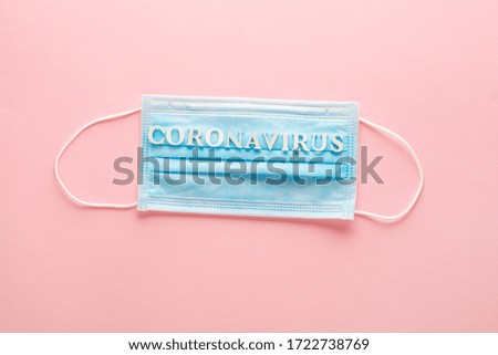 blue medical surgical protective mask to cover nose and mouth and text coronavirus on pastel pink background, top view, flat lay