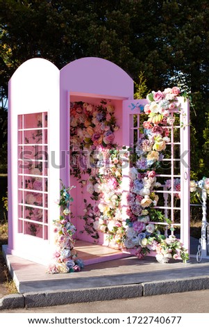 Pink phone booth decorated colourful flowers. Elegant wedding photo zone outdoor. Beautiful romantic festive place made with wooden and floral roses decorations for outside wedding ceremony in garden.