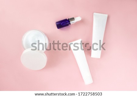 White squeeze tubes, bottle of cream, moisturizing serum in blue dropper glass flat lay on pink background top view. Mock-up template. Beauty skincare, natural cosmetic, daily products. Stock photo.