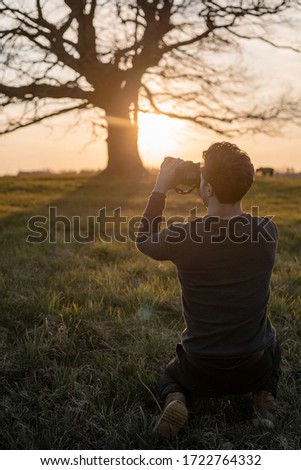 man photographs a tree at sunset.