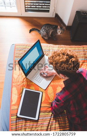 Young gingerhead woman lying bed using computer and tablet - elearning, studying, online college concept