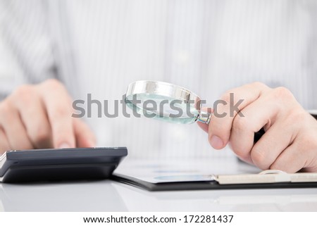 Businessman looking through a magnifying glass to documents