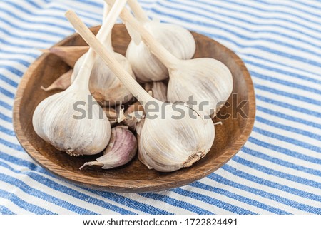 whole fresh garlic vegetable and slices on a plate standing on a striped tablecloth white and blue stripes