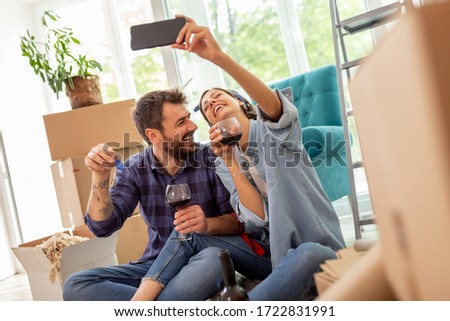 Young couple in love moving in new apartment, drinking wine and having fun taking selfies with apartment keys