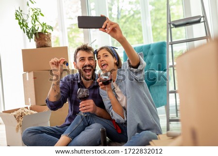 Young couple in love moving in new apartment, drinking wine and having fun taking selfies with apartment keys