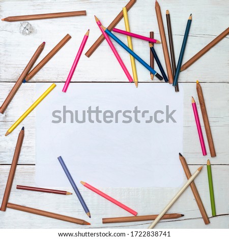 White sheet of paper around colored pencils lying on the table.