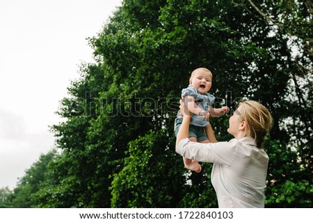 Mother throws baby in nature, girl flies in the sky. Portrait mom with child together. Mum, little daughter outdoors. Young mother with baby girl walk in park. Family holiday in garden.